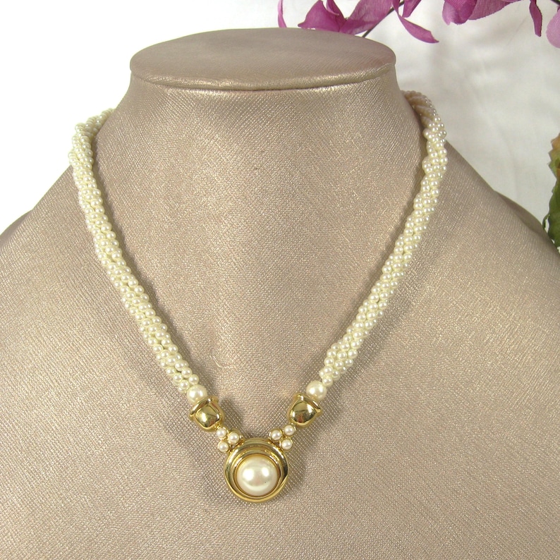 May include: A white pearl necklace with a gold pendant featuring a large pearl. The necklace is made of small, round pearls and has a simple, elegant design.
