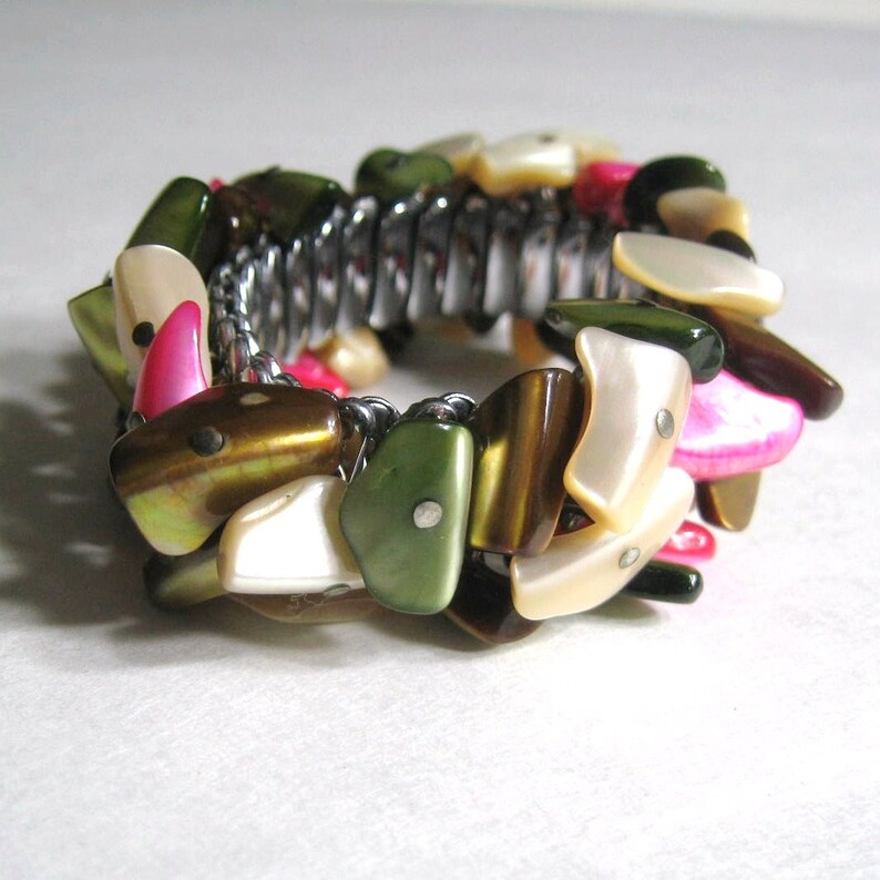 May include: A bracelet made of various colored shell pieces, including white, brown, green, and pink. The shell pieces are connected by a silver metal band.