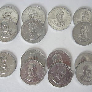 May include: A selection of silver-coloured commemorative coins, each bearing a portrait of a U.S. president. The coins show a presidential bust, the president's name, and their term years. The coins are arranged on a white surface.