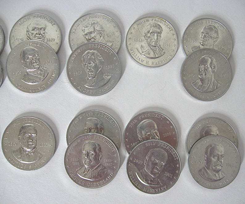 May include: A selection of silver-coloured commemorative coins, each bearing a portrait of a U.S. president. The coins show a presidential bust, the president's name, and their term years. The coins are arranged on a white surface.