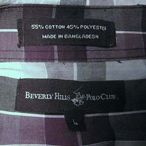 May include: Close-up of a plaid shirt label. The label reads "55% Cotton 45% Polyester Made in Bangladesh." Another label reads "Beverly Hills Polo Club" with a logo and size "L". The shirt has a purple, black, and white plaid pattern.