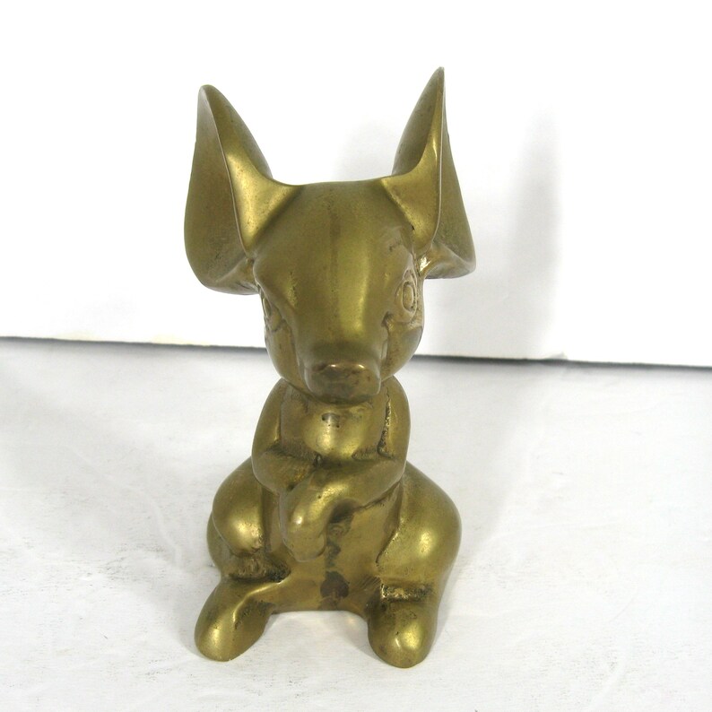 May include: A brass figurine of a mouse with large ears, sitting with its paws crossed. The mouse is a solid gold color.