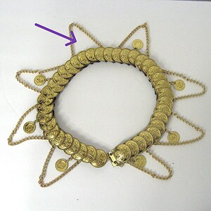 May include: A gold-colored necklace with a circular design, featuring numerous coin-like embellishments. The necklace has a star-shaped design with dangling chains and small coin pendants. The clasp is visible at the front.