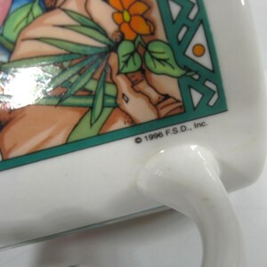 May include: White ceramic mug with a green, orange and brown design. The mug has a handle and the text "&copy; 1996 F.S.D., Inc." on the bottom.
