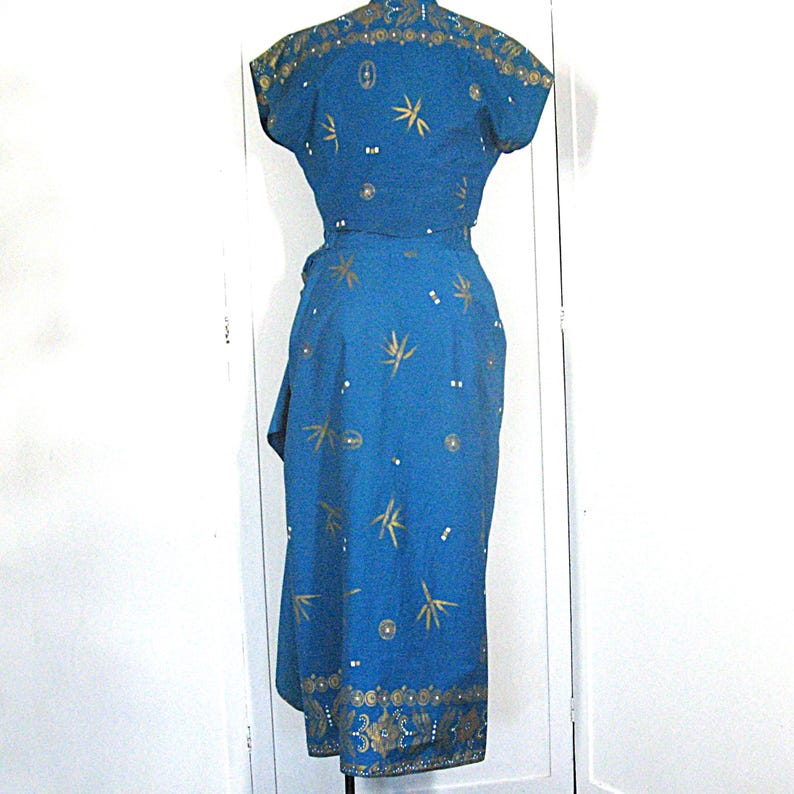 May include: A blue dress with short sleeves and a wrap-style skirt. The dress features gold-coloured bamboo and floral patterns, with decorative trim along the neckline and hem. The dress is a vintage style.