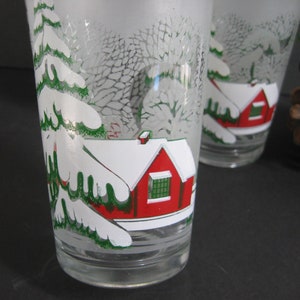 May include: Two frosted glass tumblers with a winter scene design. The scene features a red house with a white roof and a green tree covered in snow.