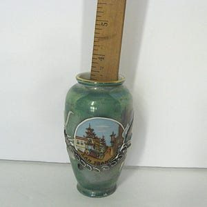 Pode incluir: Um pequeno vaso de cer&acirc;mica verde com uma cena pintada de Chinatown em S&atilde;o Francisco. O vaso tem uma borda decorativa prateada e uma r&eacute;gua de madeira no interior. O vaso tem aproximadamente 10 cm de altura.