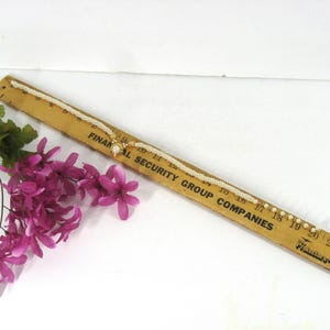 May include: A white pearl necklace with a gold pendant. The necklace is laid out on a wooden ruler with the text "Financial Security Group Companies" printed on it. The necklace is approximately 18 inches long.