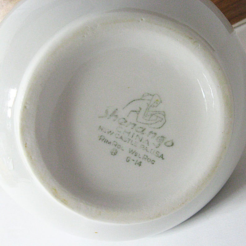 Puede incluir: Un cuenco de cer&aacute;mica blanca con un borde ligeramente ensanchado. La base del cuenco presenta un logotipo verde y el texto "Shenango China, N.W. Castle PA, USA, Rim Rol Wel Rog, G-14."