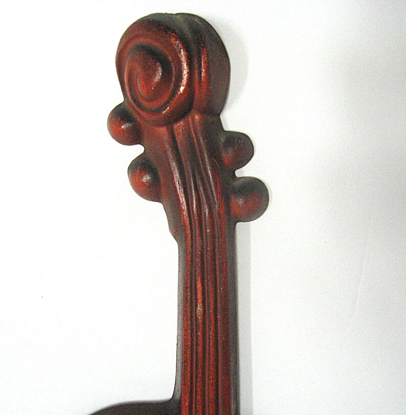 K&ouml;nnte beinhalten: Ein dunkelrotbrauner Violinhals mit Schnecke und Wirbelkasten, der oben eine geschnitzte Spiralvolute, einen schlanken Hals und vier abgerundete Wirbel an den Seiten aufweist, mit einer glatten, polierten Oberfl&auml;che und sichtbarer Holzmaserung.