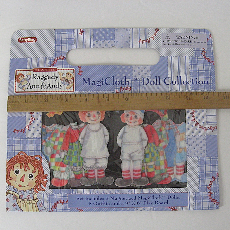 May include: A Raggedy Ann & Andy MagiCloth Doll Collection set. The package includes two magnetized dolls and eight outfits. The packaging is blue with a patchwork design and features the text "MagiCloth Doll Collection". A ruler measures 9 inches.