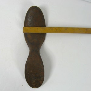 May include: A rusty metal shoe last, shaped like a foot, with a rounded toe and a narrow heel. The last is approximately 7 inches long.