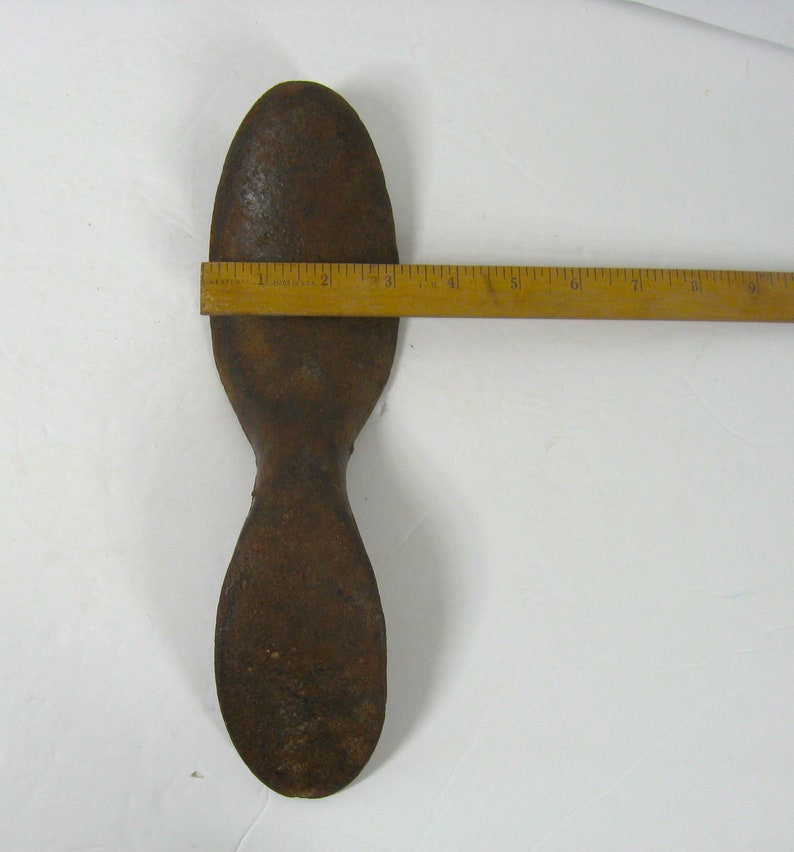 May include: A rusty metal shoe last, shaped like a foot, with a rounded toe and a narrow heel. The last is approximately 7 inches long.