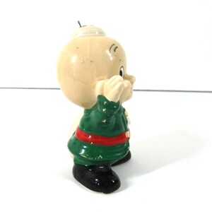 May include: A ceramic figurine of a cartoon character wearing a green and red outfit and a white hat. The character has a round head and a wide smile.