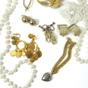 K&ouml;nnte beinhalten: Eine Sammlung von Vintage-Schmuck, darunter eine Perlenkette, goldfarbene Ohrringe, eine goldfarbene Kette mit einem silbernen Herzanh&auml;nger und eine wei&szlig;e Blumenbrosche.
