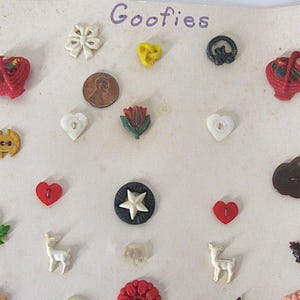 May include: A collection of assorted decorative buttons labeled Goofies, including shapes like hearts, leaves, stars, deer, and baskets in various colors. A copper penny is included for scale, measuring approximately 0.75 inches in diameter.