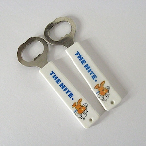 May include: Two bottle openers with white handles displaying the blue text "THE HITE". Each handle features an orange and white cartoon character. The openers have a silver metal head.