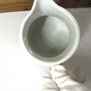 Puede incluir: Una jarra de cer&aacute;mica blanca con un pico vertedor. La jarra tiene un cuerpo redondeado y un pico en forma de asa. El interior de la jarra es de color gris claro. La jarra est&aacute; sobre una superficie blanca.
