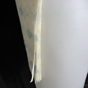 May include: A stack of off-white fabric with a blue geometric pattern. The fabric is folded and the edges are frayed.