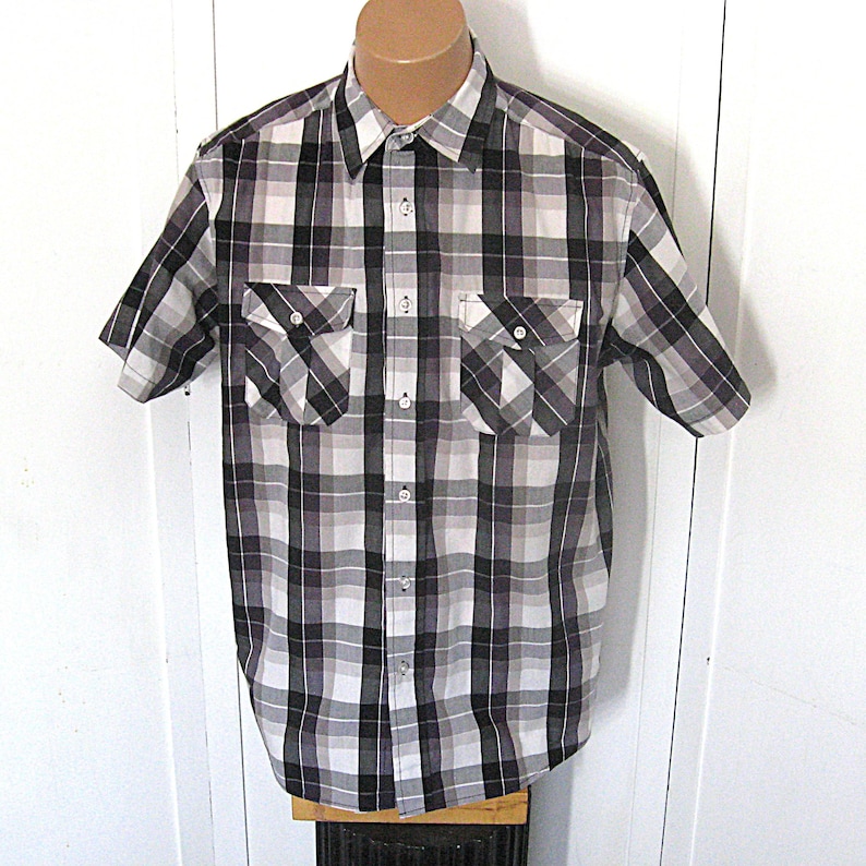 May include: A short-sleeved plaid shirt in shades of black, white, and gray. The shirt has two chest pockets and a button-down front. The plaid pattern is a classic design, suitable for casual wear.