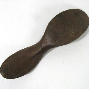 May include: A rusty metal shoe last, a tool used by shoemakers to shape and form shoes. The last is shaped like a foot and has a rounded toe and a long, narrow heel.