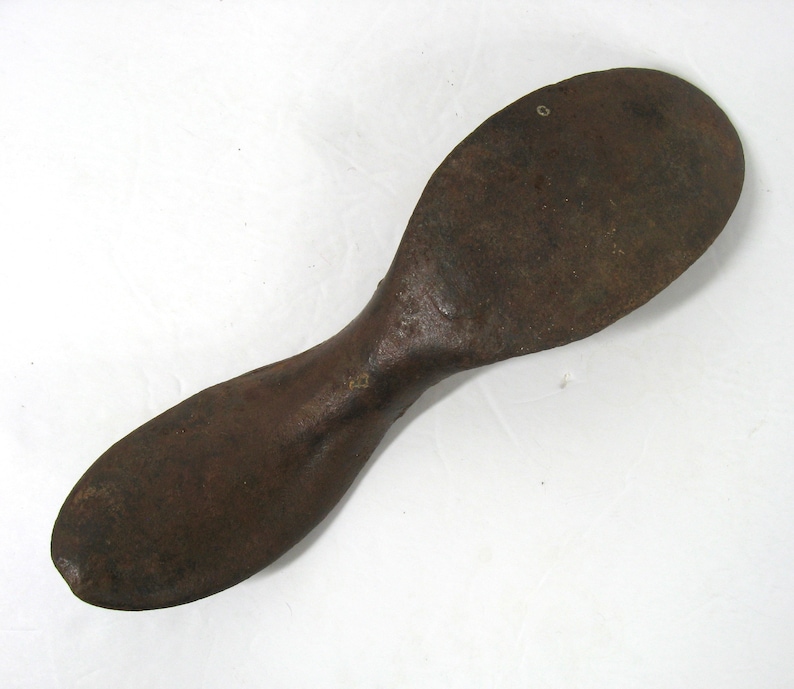 May include: A rusty metal shoe last, a tool used by shoemakers to shape and form shoes. The last is shaped like a foot and has a rounded toe and a long, narrow heel.