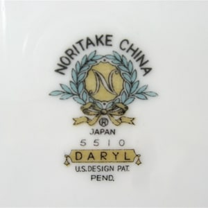 Puede incluir: Un plato de cer&aacute;mica blanco con un logotipo de Noritake China azul y dorado. El logotipo presenta una corona con la letra N en el centro. El texto "Japan 5510 Daryl U.S. Design Pat. Pend." est&aacute; impreso debajo del logotipo.