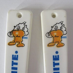 May include: Two white plastic ice cream spoons featuring a cartoon character. The character is orange and white, with a smiling face and a thumbs-up gesture. The word "WHITE" is printed in blue.