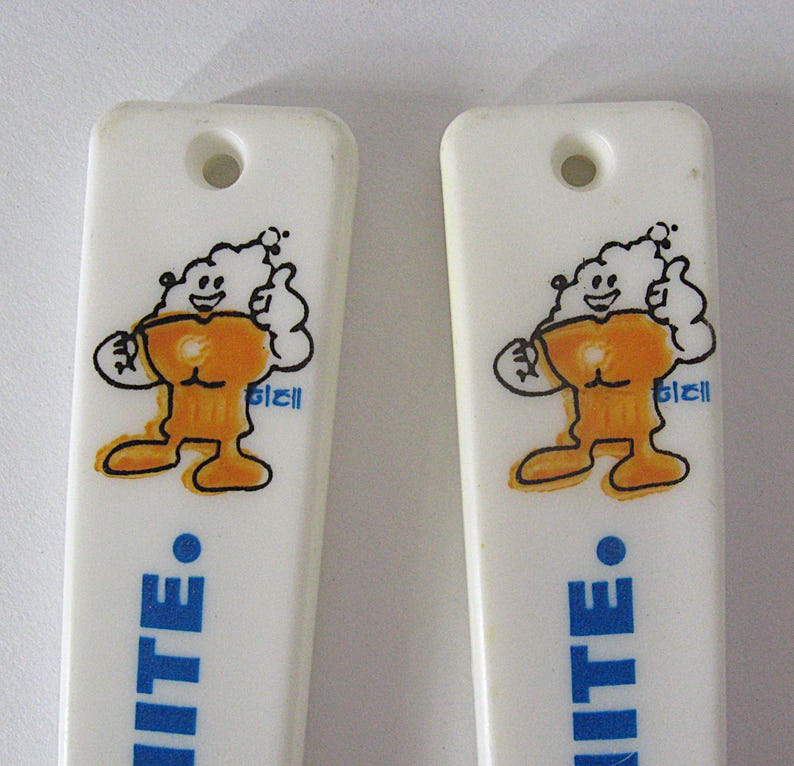 May include: Two white plastic ice cream spoons featuring a cartoon character. The character is orange and white, with a smiling face and a thumbs-up gesture. The word "WHITE" is printed in blue.