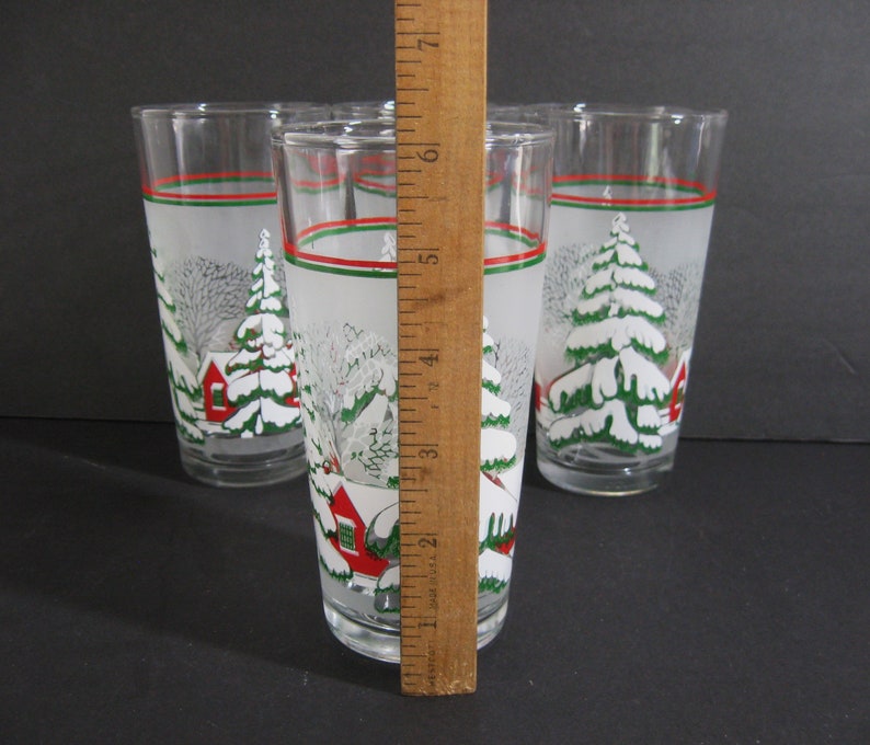 May include: Set of six frosted glass tumblers with a winter scene design. The glasses feature a white frosted background with green trees, red houses, and white snow. The glasses have a red and green stripe around the top.