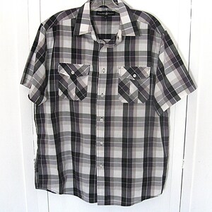 May include: A short-sleeved plaid shirt in shades of gray, black, and white. The shirt features two chest pockets with button closures and a classic collar. The fabric has a checkered pattern.