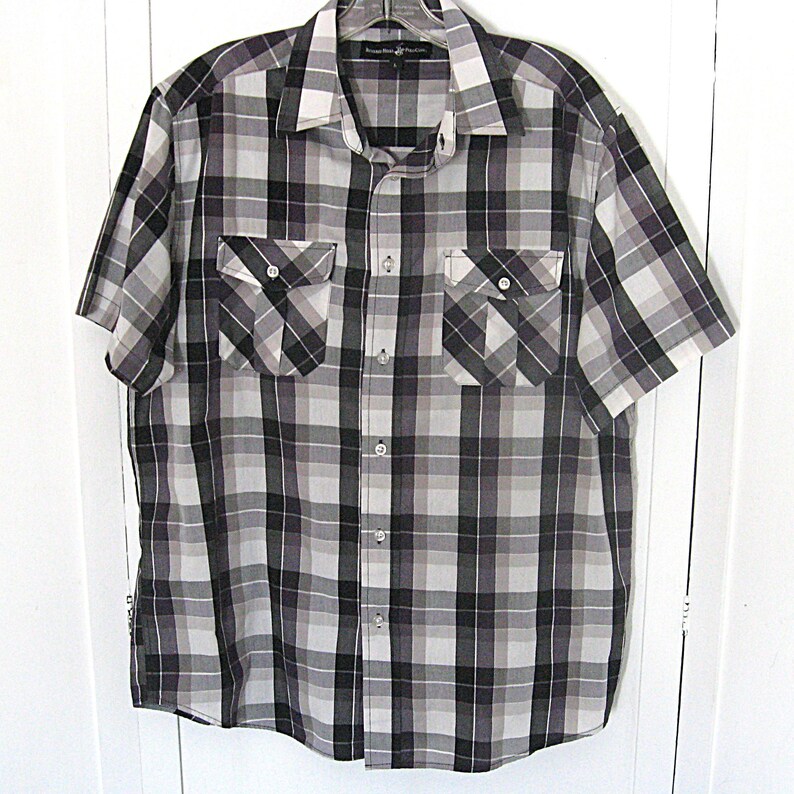 May include: A short-sleeved plaid shirt in shades of gray, black, and white. The shirt features two chest pockets with button closures and a classic collar. The fabric has a checkered pattern.