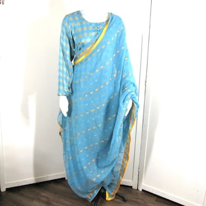 May include: A light blue and gold patterned saree with a matching light blue and white checkered blouse. The saree has a gold trim and is draped over a mannequin.