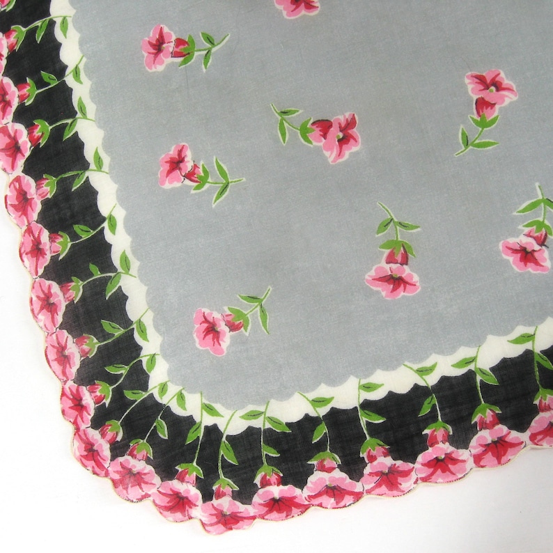 Pode incluir: Um len&ccedil;o vintage com fundo cinza e uma borda festonada preta e branca. O len&ccedil;o &eacute; decorado com flores cor-de-rosa.