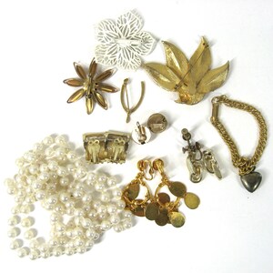 K&ouml;nnte beinhalten: Eine Sammlung von Vintage-Schmuck, darunter eine Perlenkette, goldfarbene Ohrringe, ein goldfarbenes Armband und mehrere Broschen. Die Broschen haben die Form einer Blume, eines Blattes und eines Sterns.