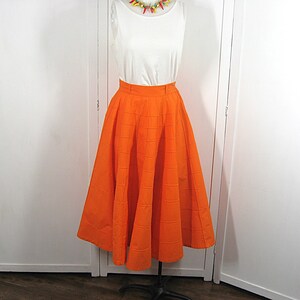 May include: A bright orange full skirt with a gathered waistline. The skirt is made of a textured fabric and has a midi length.