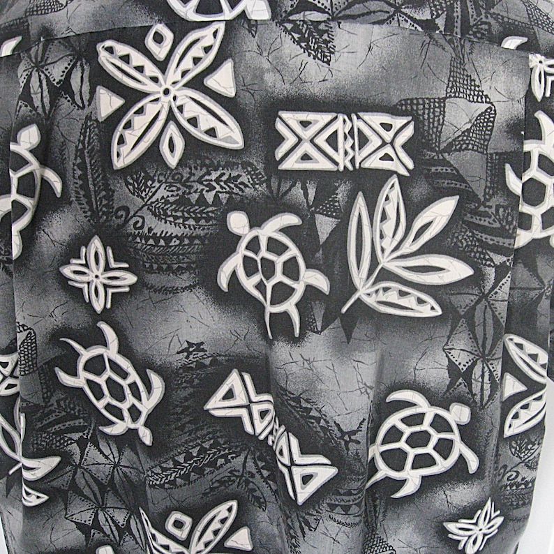 May include: A button-down shirt featuring a monochromatic black, gray, and white print. The pattern consists of stylized sea turtles, geometric shapes, and leaf-like motifs set against a textured, mottled background with a batik-style aesthetic.