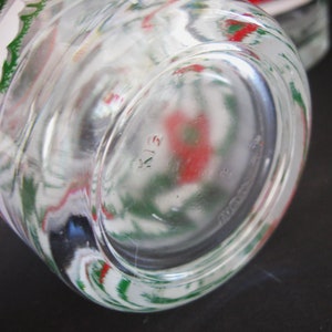 May include: Close-up of the bottom of a clear glass jar with a green and red floral design. The bottom of the jar has a circular design with the number "413" printed on it.