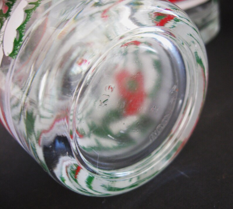 May include: Close-up of the bottom of a clear glass jar with a green and red floral design. The bottom of the jar has a circular design with the number "413" printed on it.