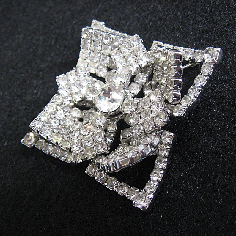 May include: A silver-tone brooch featuring a large, clear rhinestone centre surrounded by smaller rhinestones. The brooch is shaped like a bow.