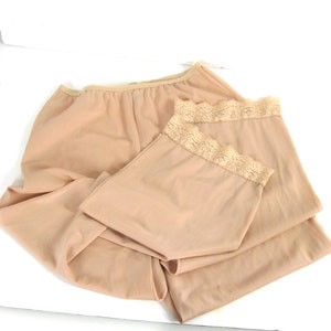 May include: Two pairs of nude-colored slip shorts with lace trim. The shorts are made of a soft, stretchy fabric and are perfect for layering under dresses or skirts.