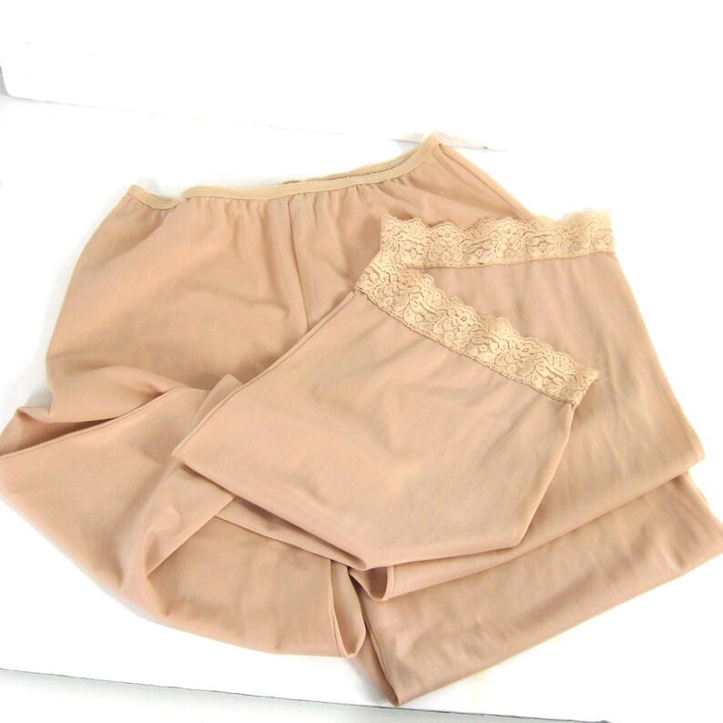 May include: Two pairs of nude-colored slip shorts with lace trim. The shorts are made of a soft, stretchy fabric and are perfect for layering under dresses or skirts.