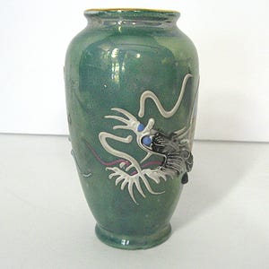 Pode incluir: Vaso de cer&acirc;mica verde com um design detalhado de drag&atilde;o. O drag&atilde;o &eacute; branco com detalhes em preto e olhos azuis. O vaso tem uma borda dourada e uma superf&iacute;cie texturizada, de inspira&ccedil;&atilde;o asi&aacute;tica.