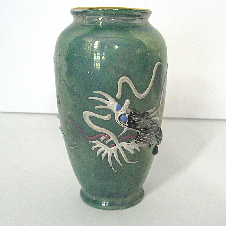 Pode incluir: Vaso de cer&acirc;mica verde com um design detalhado de drag&atilde;o. O drag&atilde;o &eacute; branco com detalhes em preto e olhos azuis. O vaso tem uma borda dourada e uma superf&iacute;cie texturizada, de inspira&ccedil;&atilde;o asi&aacute;tica.