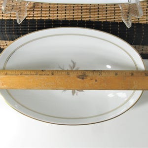 Puede incluir: Plato ovalado blanco para servir con borde dorado y un dise&ntilde;o floral en el centro. El plato mide 25,4 cm de largo.