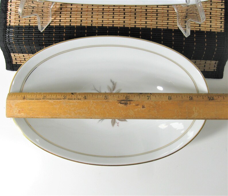 Puede incluir: Plato ovalado blanco para servir con borde dorado y un dise&ntilde;o floral en el centro. El plato mide 25,4 cm de largo.