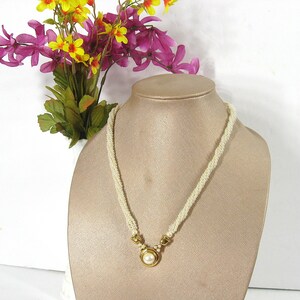 May include: A white pearl necklace with a gold pendant featuring a large pearl. The necklace is displayed on a white mannequin bust.