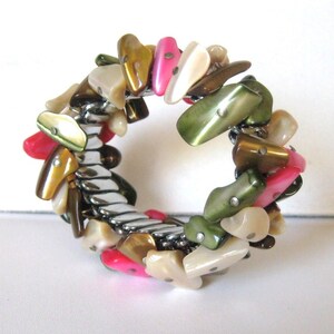 May include: A silver expandable bracelet with a variety of colorful shell-shaped beads. The beads are in shades of pink, green, brown, and white.