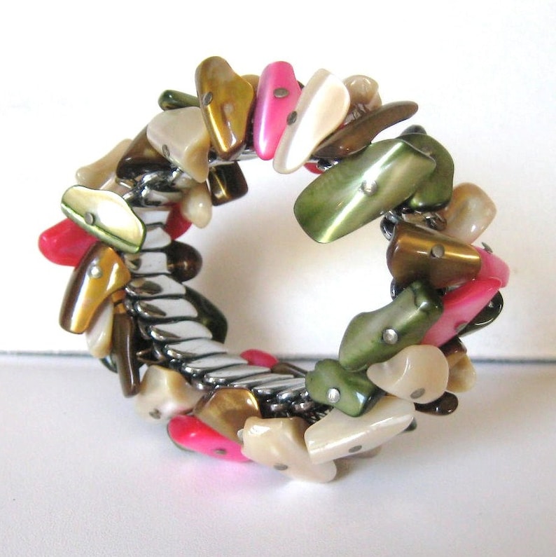 May include: A silver expandable bracelet with a variety of colorful shell-shaped beads. The beads are in shades of pink, green, brown, and white.