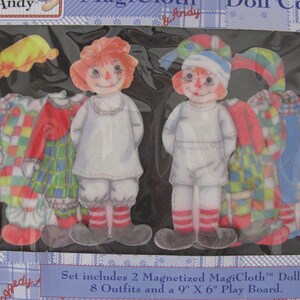 May include: A boxed set featuring two magnetized dolls and eight outfits. The dolls have red yarn hair, painted faces, and wear white outfits with red and white striped socks. The outfits include dresses and hats in various colors and patterns. The text on the box reads "Ann & Andy".